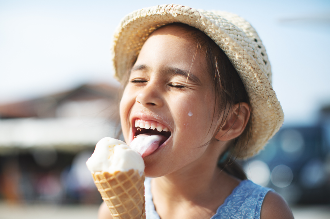 A little girl happily licking a vanillia ice cream cone.